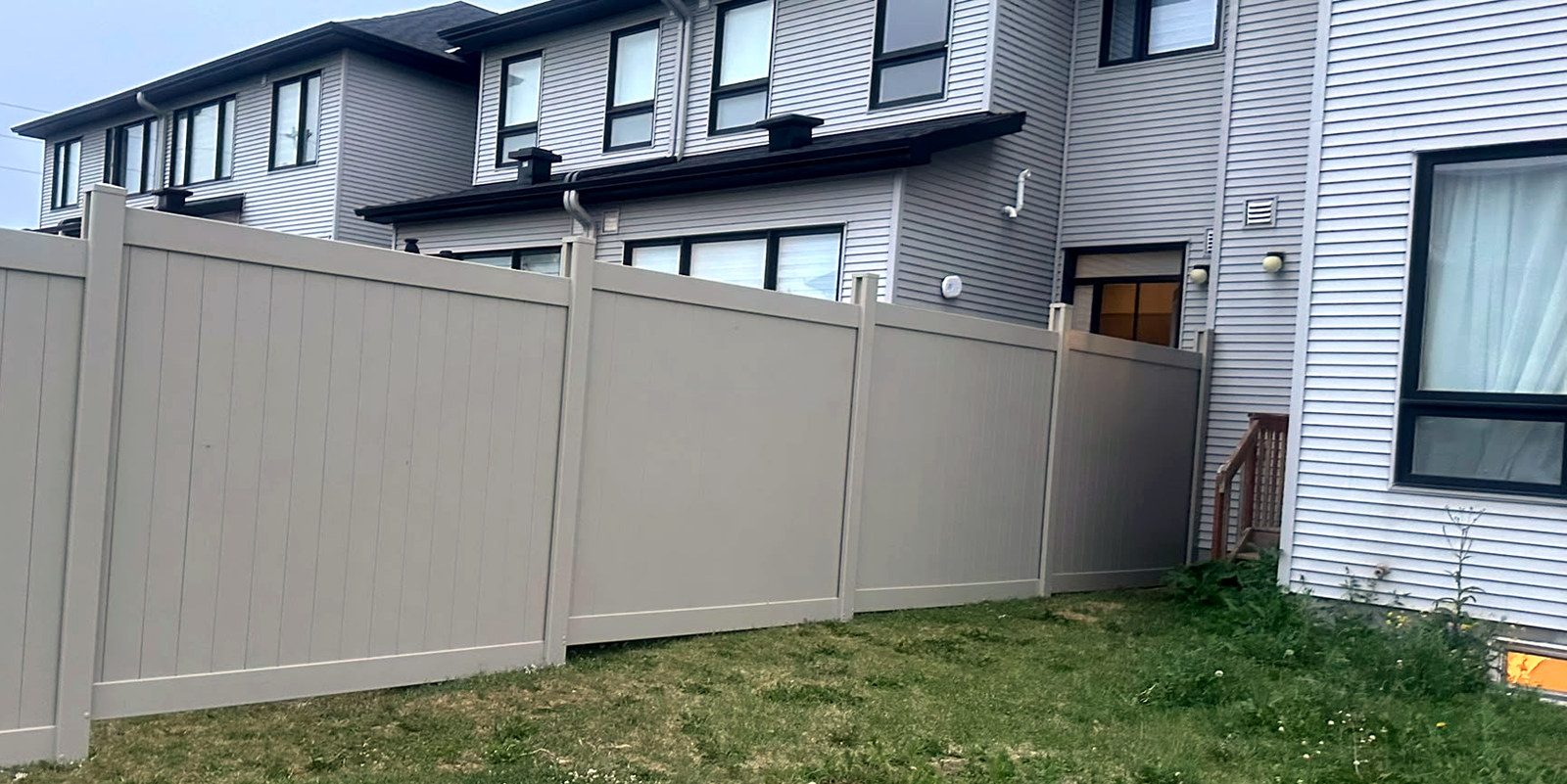 An Adobe PVC fence running along the back of a row of townhouses, stepping down as the ground falls away.